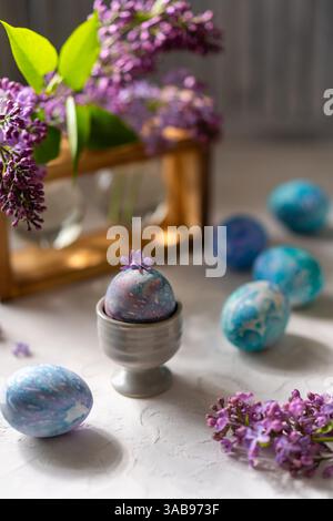 Vibrant Easter eggs are artistically hand painted displayed with fresh lilac blooms on a textured white surface. Perfect for adding a touch of spring Stock Photo