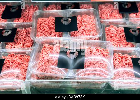 Neatly packed minced meat trays are displayed on a refrigerated supermarket shelf. Each tray is wrapped in clear plastic and labeled with a cow silhou Stock Photo