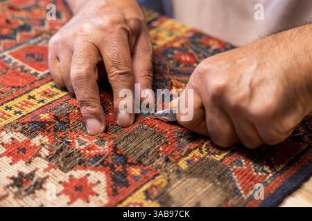Cropped unrecognizable senior master craftsman from Iran meticulously restores a vibrant, traditional carpet in his workshop located in Salzburg, Aust Stock Photo