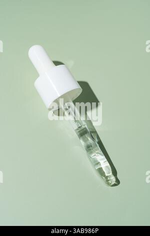 A single pipette dropper filled with a clear liquid, oriented diagonally, presented on a soothing mint green background, casting a soft shadow. Stock Photo