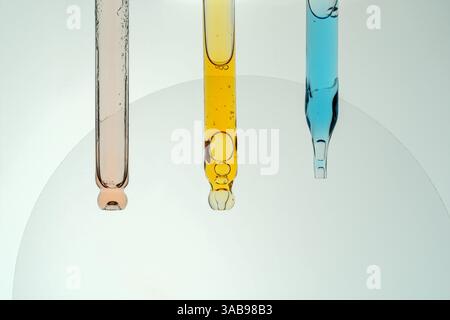 Three pipettes filled with colorful liquids are shown in close up. The liquids are orange, blue, and light pink, representing cosmetic exploration. Stock Photo