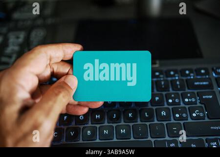 A hand holds a blank card over a laptop keyboard, symbolizing online shopping, identity verification, and business branding. Ideal for technology and Stock Photo