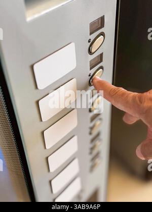 A close-up view of a person's hand pressing a button on an elevator panel. The panel features several buttons arranged vertically, highlighting a mode Stock Photo