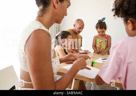 A family sitting together around a table, engaging in creative activities and crafts. The parents and children are focused and enjoying quality time a Stock Photo