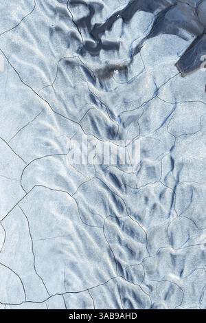 A striking aerial view of icy terrain showcasing natural patterns and textures. The surface appears cracked and textured, with subtle shades of blue a Stock Photo