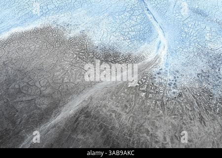 A stunning aerial view showcases intricate patterns of cracked earth and icy formations, blending shades of blue, gray, and white, creating an abstrac Stock Photo