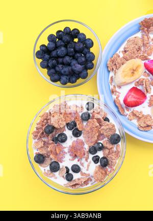 A vibrant breakfast setting featuring bowls of cereal with milk, topped with fresh blueberries, strawberries, and bananas. Complemented with a side bo Stock Photo