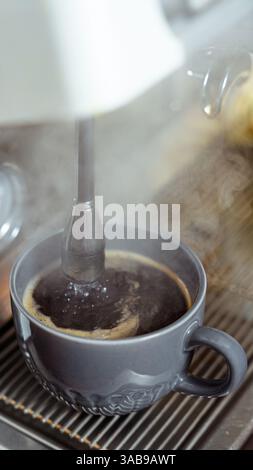 Steaming shot of rich black coffee in a gray ceramic cup, brewed on an espresso machine. Captures the essence of cafe culture and morning routines. Stock Photo