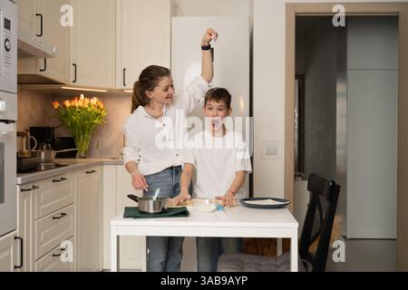 A joyful mother and son bake in a modern kitchen, sharing a fun moment. The child looks surprised as they prepare ingredients together, surrounded by Stock Photo