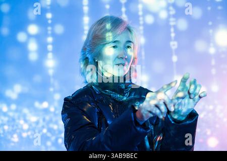 An elderly Asian woman navigates a vibrant virtual metaverse environment, showcasing the intersection of technology and age as she interacts with digi Stock Photo