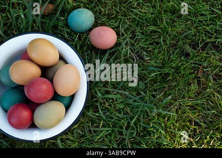 A collection of vibrant Easter eggs sits in a white bowl on lush green grass, capturing the essence of spring festivities and outdoor celebrations. Stock Photo