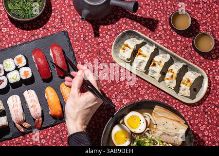 Top-down view of a vibrant Japanese meal, where a hand using chopsticks interacts with the food, enhancing the sense of authenticity and dining experi Stock Photo