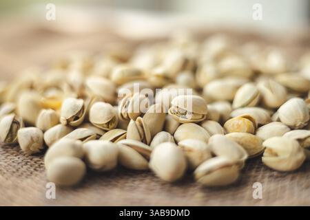 A close up image of shelled pistachios scattered on burlap, showcasing their natural texture. The soft focus background adds depth, highlighting the s Stock Photo
