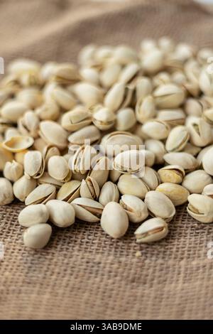 A pile of pistachios lies scattered on a rustic burlap surface, showcasing their textured shells. The focus on the nuts highlights the natural texture Stock Photo