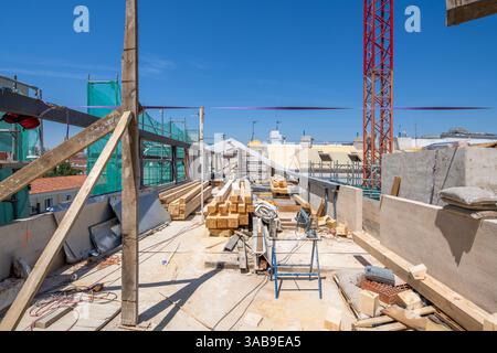 A bustling construction site with timber, tools, and equipment strewn across the floor. Scaffolding and a red crane outline the backdrop under a brigh Stock Photo