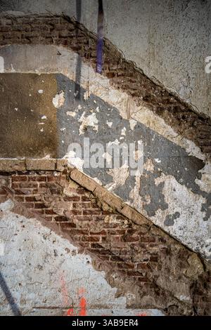 A close-up of an old wall under renovation, revealing layers of peeling plaster and exposed brick. The worn textures and faded paint highlight the pas Stock Photo