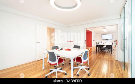 A modern office featuring an open layout with white walls and wooden floors. Stylish chairs and tables, accentuated with red decor, create a vibrant w Stock Photo