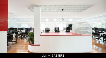 A modern office interior with an open workspace, featuring sleek black chairs, wooden flooring, and vibrant red accents. Ambient lighting enhances the Stock Photo