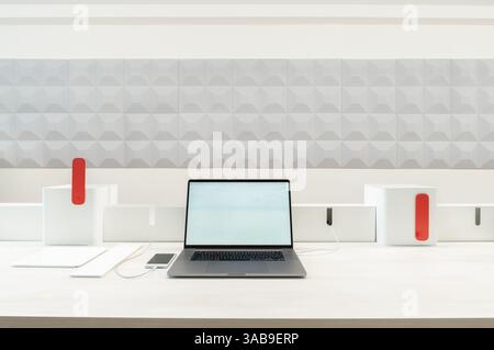 A sleek workspace in office featuring a laptop, smartphone, and tablet. The minimalist design is enhanced by a geometric patterned wall and clean line Stock Photo