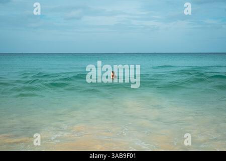 A young woman enjoys a swim in the clear turquoise waters of a tranquil beach in vacation, creating a peaceful scene with gentle waves, sandy shores, Stock Photo