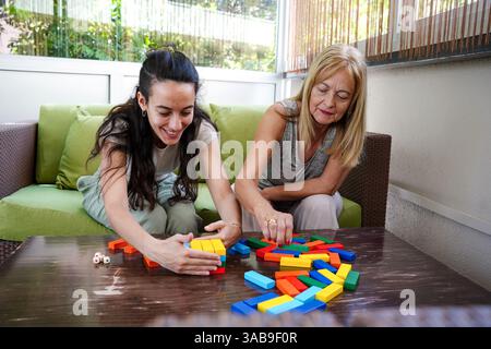 A joyful moment as a mother and daughter engage in a colorful board game. Smiling and focused, they enjoy quality time at home, strengthening their bo Stock Photo