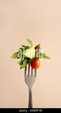 A close up image of various fresh salad ingredients including avocado, cherry tomato, arugula, and a raisin elegantly arranged on a silver fork over a Stock Photo