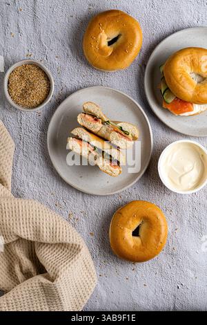 Top view of a selection of bagels with smoked salmon, cream cheese, and toppings. Bagels are displayed on plates with a textured cloth background, cre Stock Photo