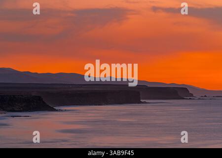 A stunning sunset over the rugged coastline of Fuerteventura in the Canary Islands, Spain. The deep orange sky contrasts beautifully with the dark sil Stock Photo