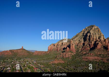 A breathtaking view of Sedona, Arizona, showcasing its iconic red rock formations set against a clear blue sky with a residential area below. Stock Photo