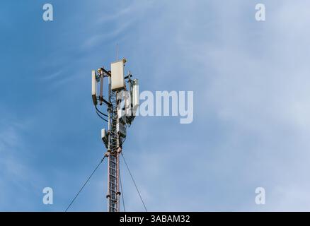 The top of a tall mast with mobile cellular antennas against a blue sky Stock Photo