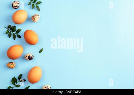 Brown and quail eggs with green leaves on blue background. Easter concept. Top view, flat lay, copy space. Stock Photo