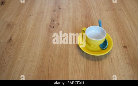 Yellow Ceramic Espresso Coffee Cup, Blue Spoon on Wooden Table. Caffee Concept. sits on a matching saucer with a blue spoon, placed on a wooden table. Stock Photo