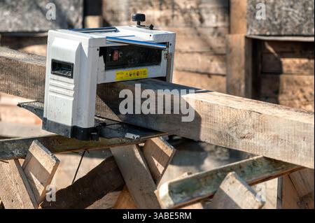A wood planer is precise sanding and shaping lumber on a bright sunny day at a workshop. Stock Photo