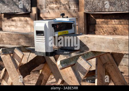 Tool is smoothing a wooden plank on a worktable outside under clear blue skies Stock Photo