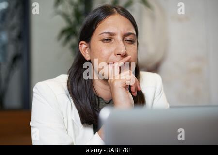 Focused Woman Deep in Thought While Looking at Laptop in Modern Office Setting Stock Photo