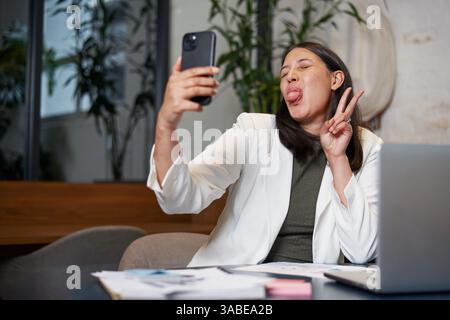 Professional Woman Taking a Fun Selfie While Sitting in a Modern Office Workspace Stock Photo