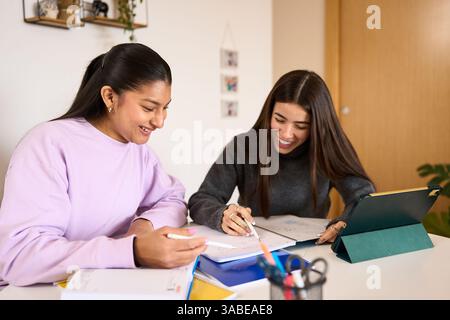 Two happy students studying together with a digital tablet and notebooks, smiling and collaborating on their homework Stock Photo