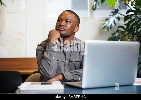 Professional Man in Gray Shirt Reflecting at Work Desk in Modern Office Workspace Stock Photo