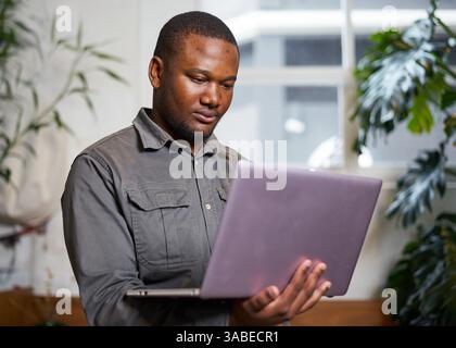 Young Professional Using Laptop in Modern Office with Natural Light and Greenery Stock Photo