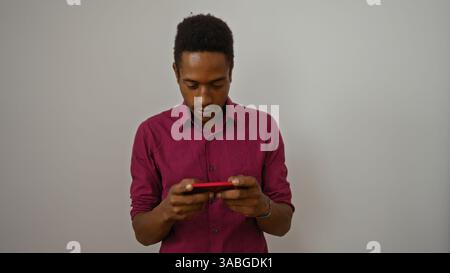 Young man wearing red shirt focused on smartphone against a plain white background Stock Photo