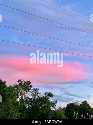 A mesmerizing sunset sky painted in soft pink, blue, and purple hues, resembling cotton candy, while the moon is visible in the evening sky. Stock Photo
