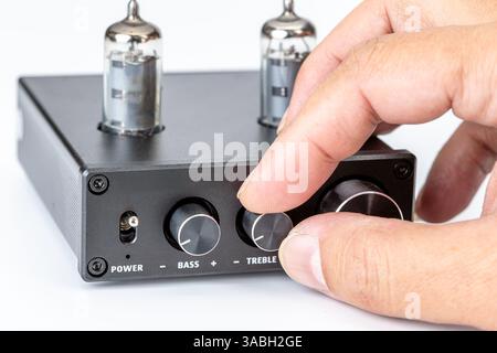 Fine tuning of a vacuum tube amplifier: Focused image of a person adjusting the treble knob on a black amplifier, emphasizing precision and control. Stock Photo