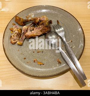 used dinner plates with spoons, forks and the remains of used chicken bones Stock Photo