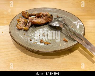 used dinner plates with spoons, forks and the remains of used chicken bones Stock Photo