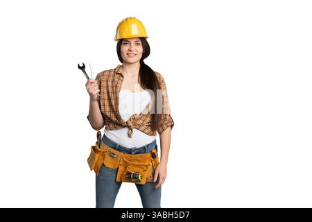 Happy female construction worker wearing a yellow hard hat and tool belt, holding wrenches with confidence, representing skill and expertise in repair Stock Photo