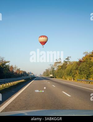Point of view: driving on empty highway in left lane. Car with cruise control driving on straight road while balloon aerostat hovering above it. Stock Photo