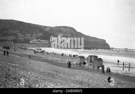 circa 1930s, historlcal picture showing the beach, with changing huts on wheels, at Llandudno, Wales. The Grand Hotel, Pavilion and the long pier can be seen in the distance. The Welsh seaside resort was known as the 'the Queen of the Welsh Watering Places'. Stock Photo