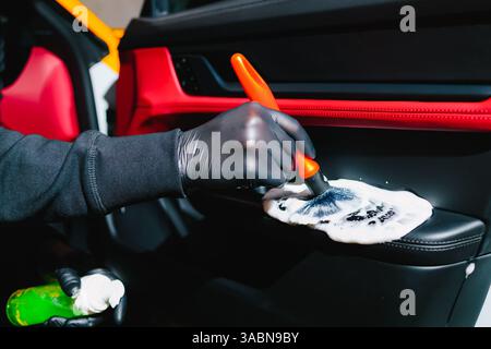 Process of removing dust and dirt from the car door panel at the carwash. Car detailer cleans the auto door with foam brush and detergent Stock Photo