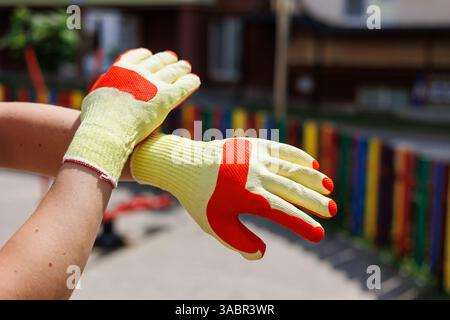 Vibrant yellow and orange protective gloves displayed in a sunny outdoor setting, perfect for various trades. Ideal for landscape, construction, and g Stock Photo