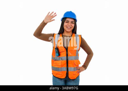 Young latin woman architect or engineer wearing protective equipment smiling and waving on white background, representing construction industry and fe Stock Photo